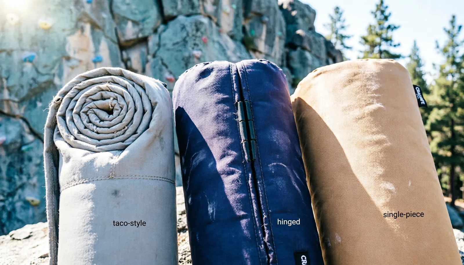 Various types of bouldering crash pads displayed side by side at an outdoor climbing area.